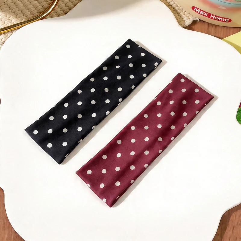 Ein dunkelrotes Polka-Dot-Stoff-Haarreif ist diagonal auf einer weißen Oberfläche gelegt.