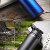A black leakproof portable aluminum water bottle is shown resting on a wooden surface with green foliage in the background.