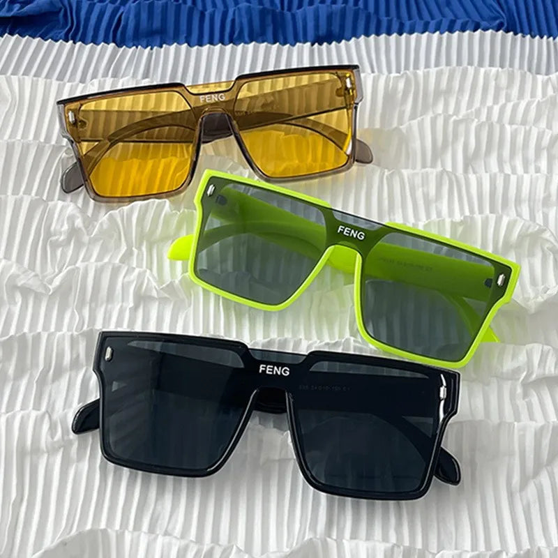 Three pairs of square sunglasses in amber, lime green, and black resting on white crinkled paper.