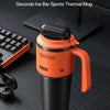An orange insulated thermal mug with a black lid and handle is shown on a dark surface.