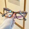 A hand holds a pair of tortoiseshell-patterned blue light blocking eyeglasses.