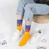 A pair of yellow novelty socks with a flame pattern are displayed next to white sneakers.