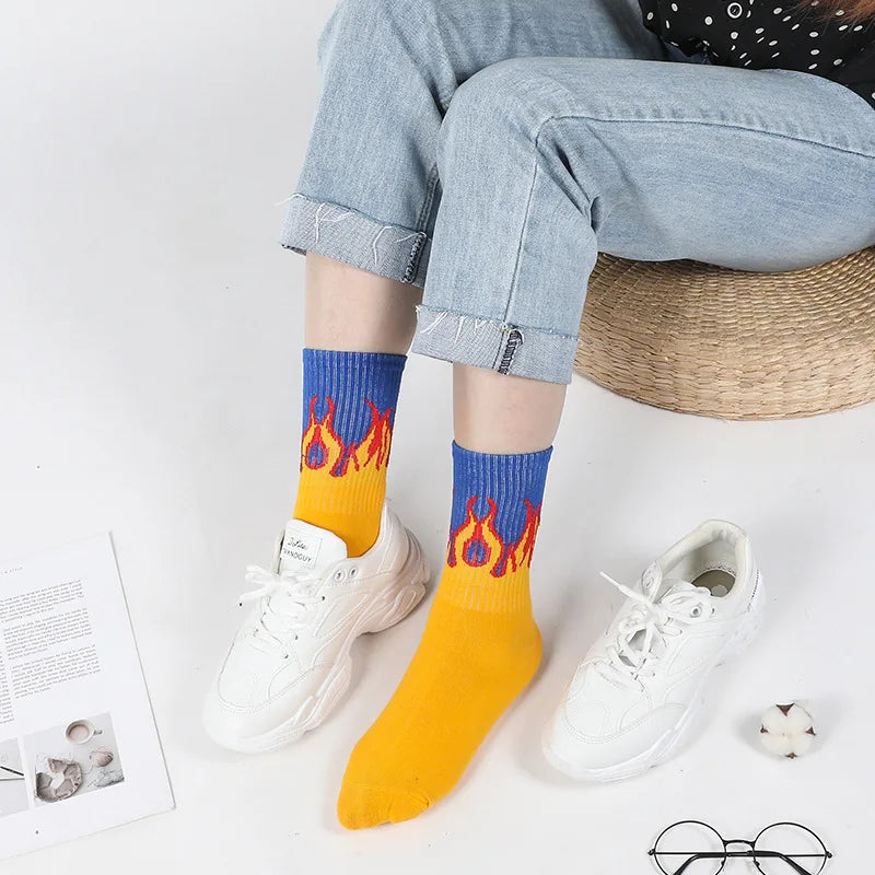 A pair of yellow novelty socks with a flame pattern are displayed next to white sneakers.