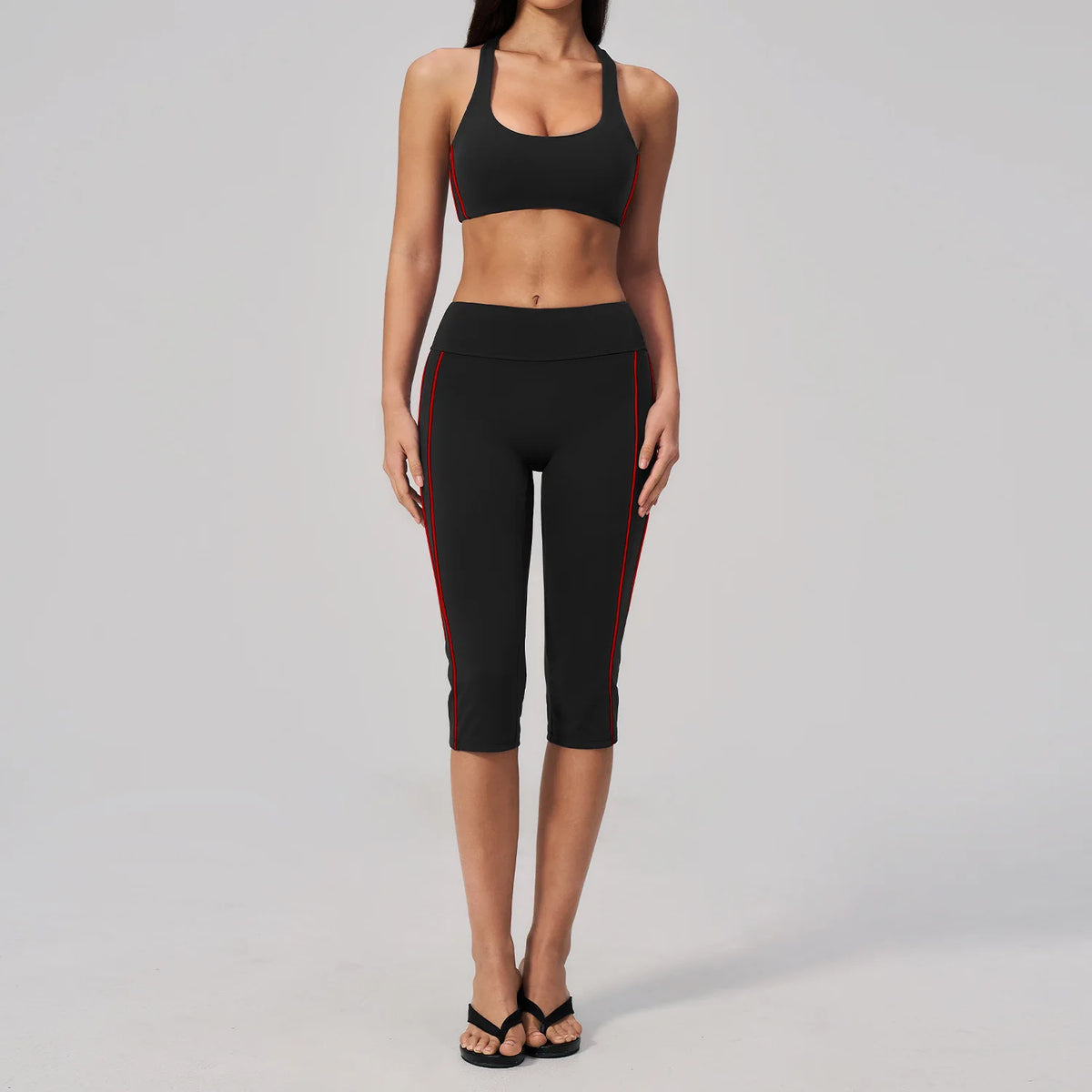 A woman models a black two-piece yoga and sports tracksuit set with red trim.