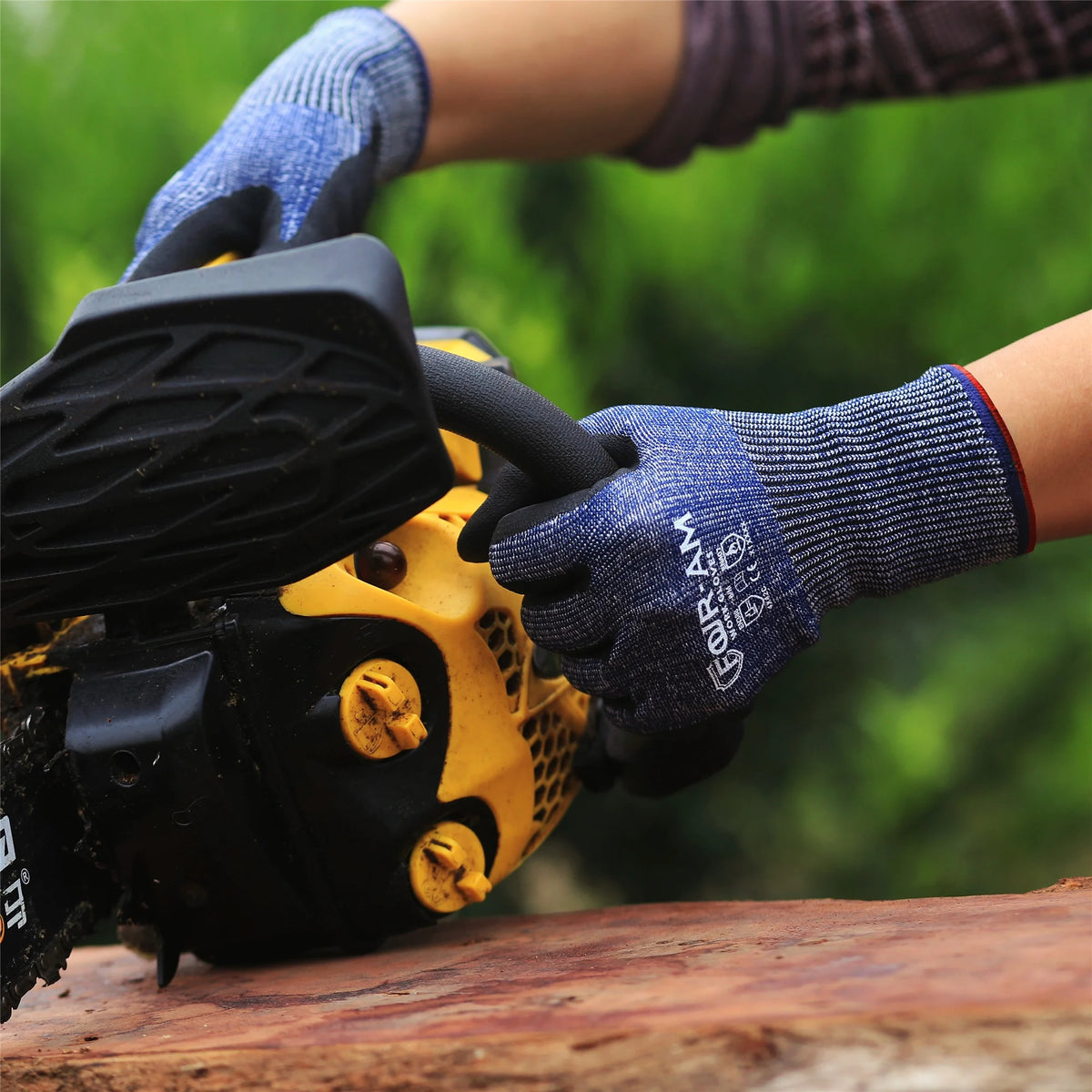 A hand wearing blue work gloves is operating a yellow power tool, with green foliage in the blurred background.