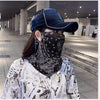 Una persona vistiendo una bufanda protectora UV negra con estampado paisley y máscara, con una gorra de béisbol azul oscuro, 
