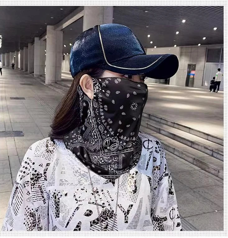 Una persona vistiendo una bufanda protectora UV negra con estampado paisley y máscara, con una gorra de béisbol azul oscuro, 