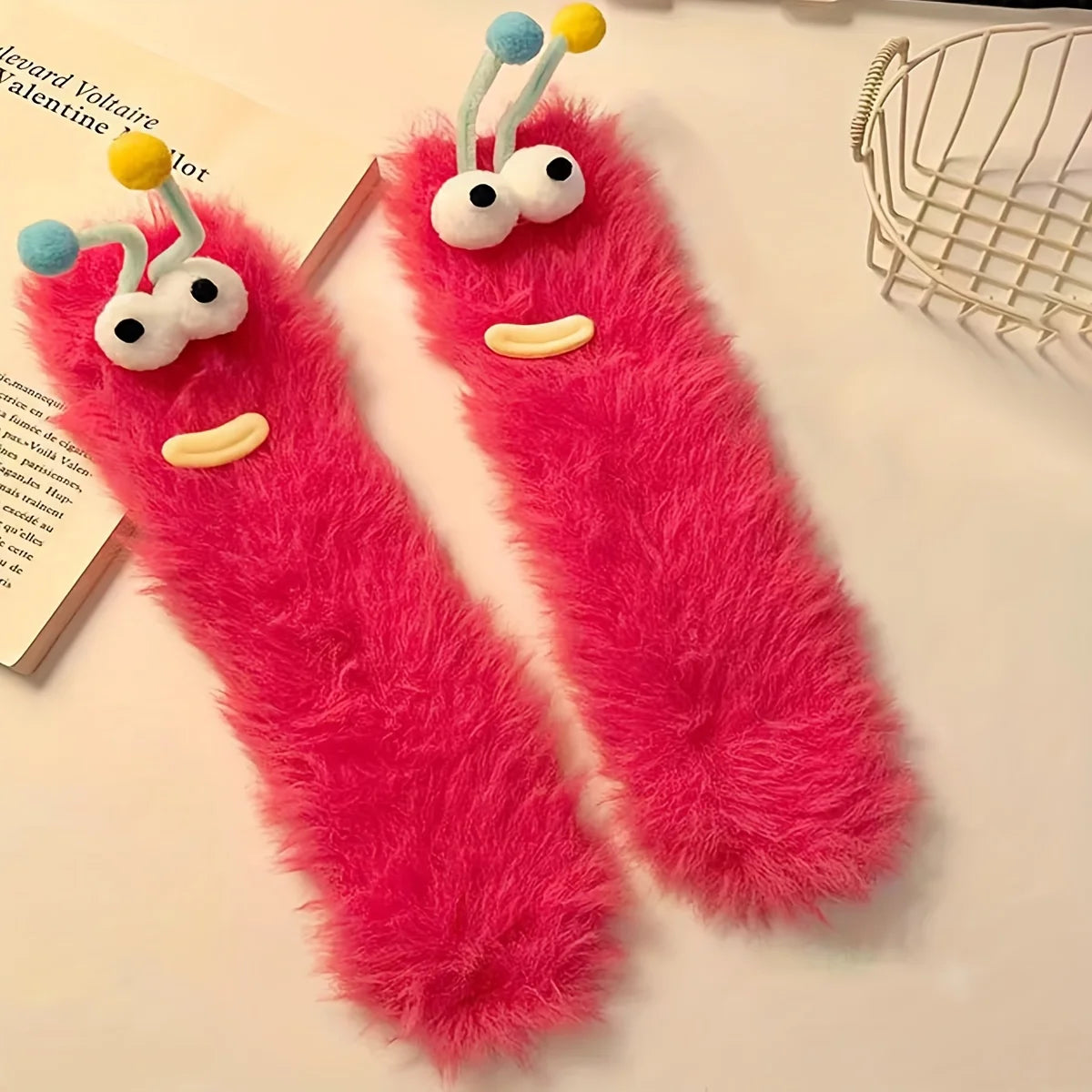 Pair of bright pink plush caterpillar floor socks with yellow and blue accents