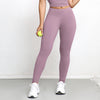 A woman wearing mauve high-waisted sports leggings and a purple top stands indoors.