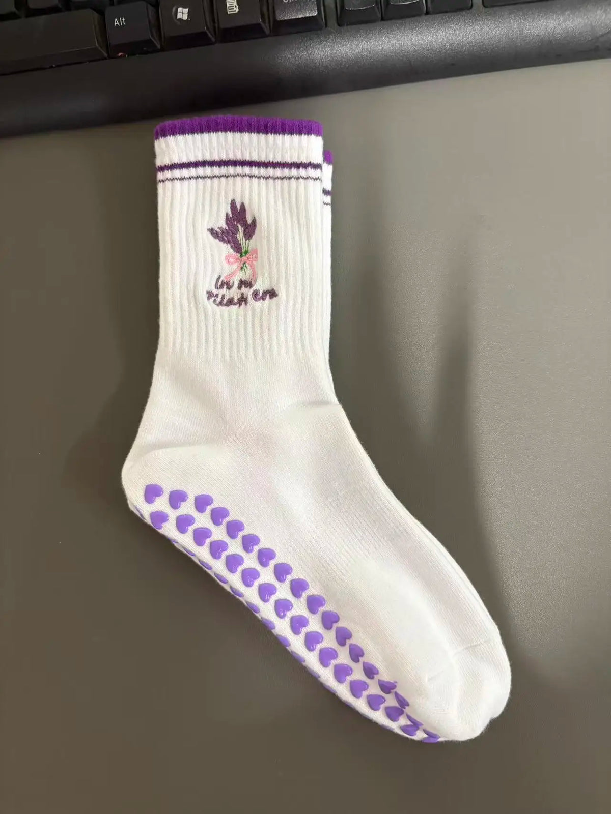 Weiße Strick-Yoga-Socken mit lila Zierrand und kleiner Blumenstickerei an der Zehe.
