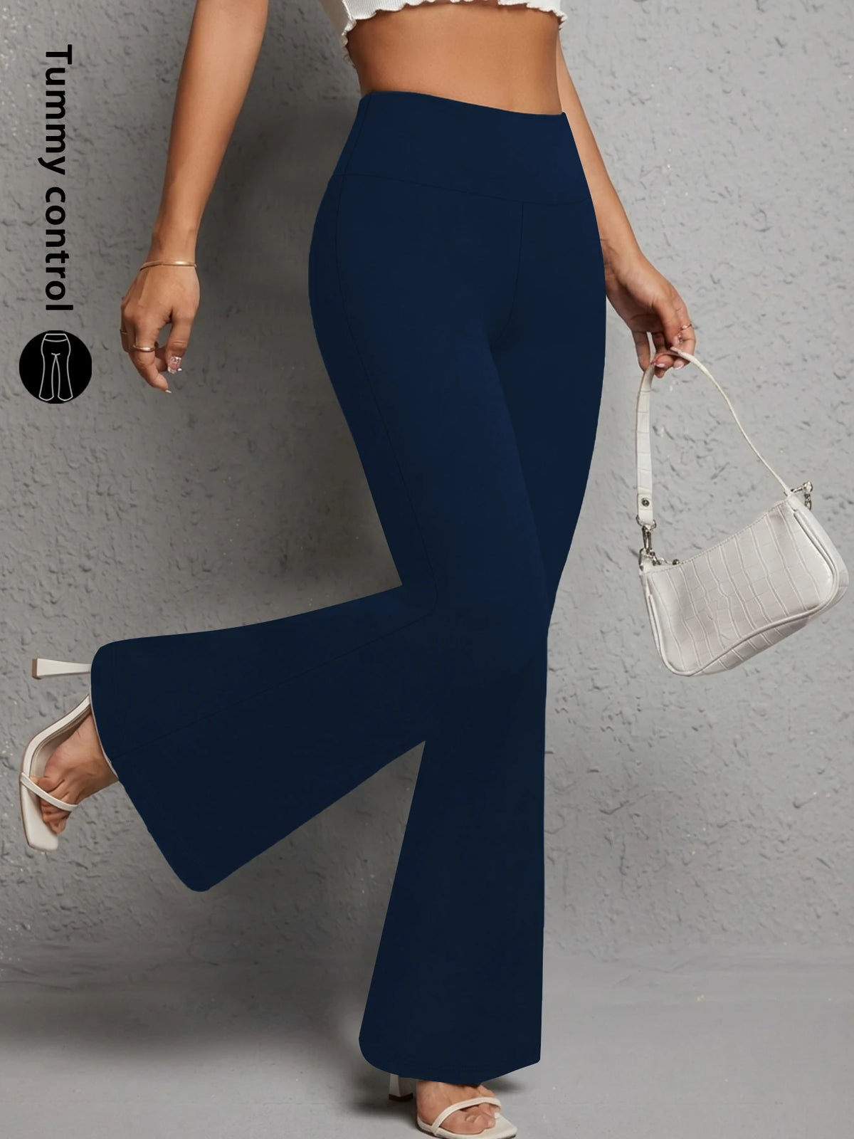 A woman wearing navy blue flared yoga trousers and a white bag, demonstrating tummy control.