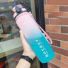 Eine Hand hält eine verlustige isolierte Wasserflasche mit rosa und blauen Akzenten vor einem Backstein-Hintergrund.