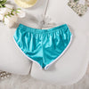 Ein Paar tealblauer Satin-Trainingsshorts mit floralen Akzenten auf einer weißen Oberfläche.