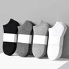 Un juego de tres calcetines de algodón unisex transpirables en negro, gris y blanco dispuestos sobre una superficie clara.