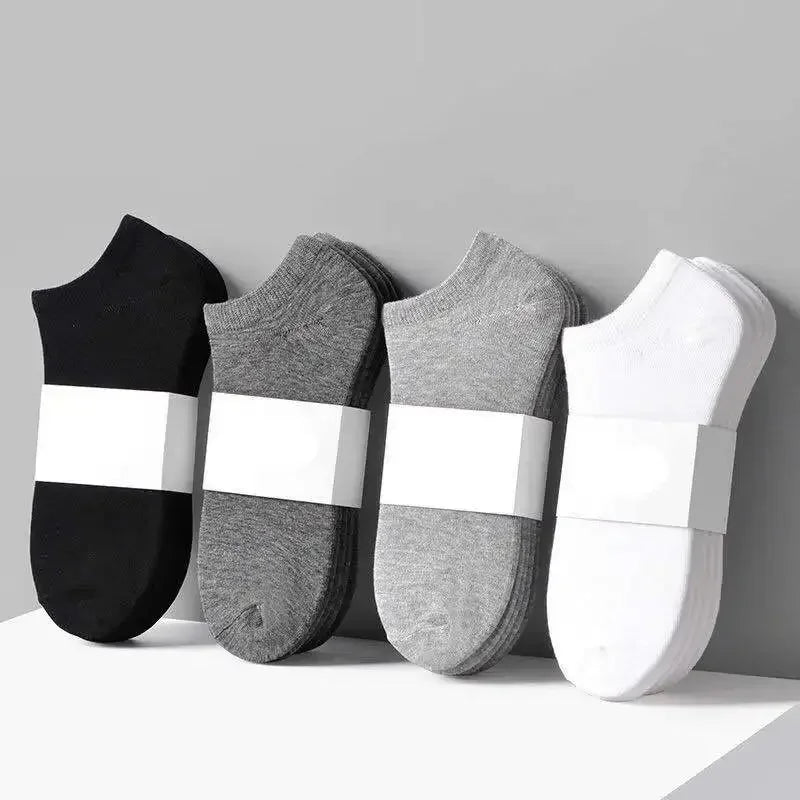 Un juego de tres calcetines de algodón unisex transpirables en negro, gris y blanco dispuestos sobre una superficie clara.