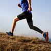 A person wearing a blue shirt and black compression leggings runs outdoors on a dry, grassy hill.