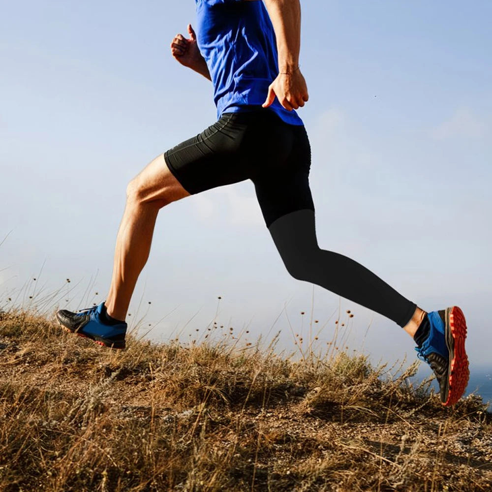 A person wearing a blue shirt and black compression leggings runs outdoors on a dry, grassy hill.