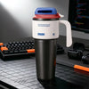 A black insulated tumbler with a white lid, red accent, and handle sits on a dark desk next to a keyboard.