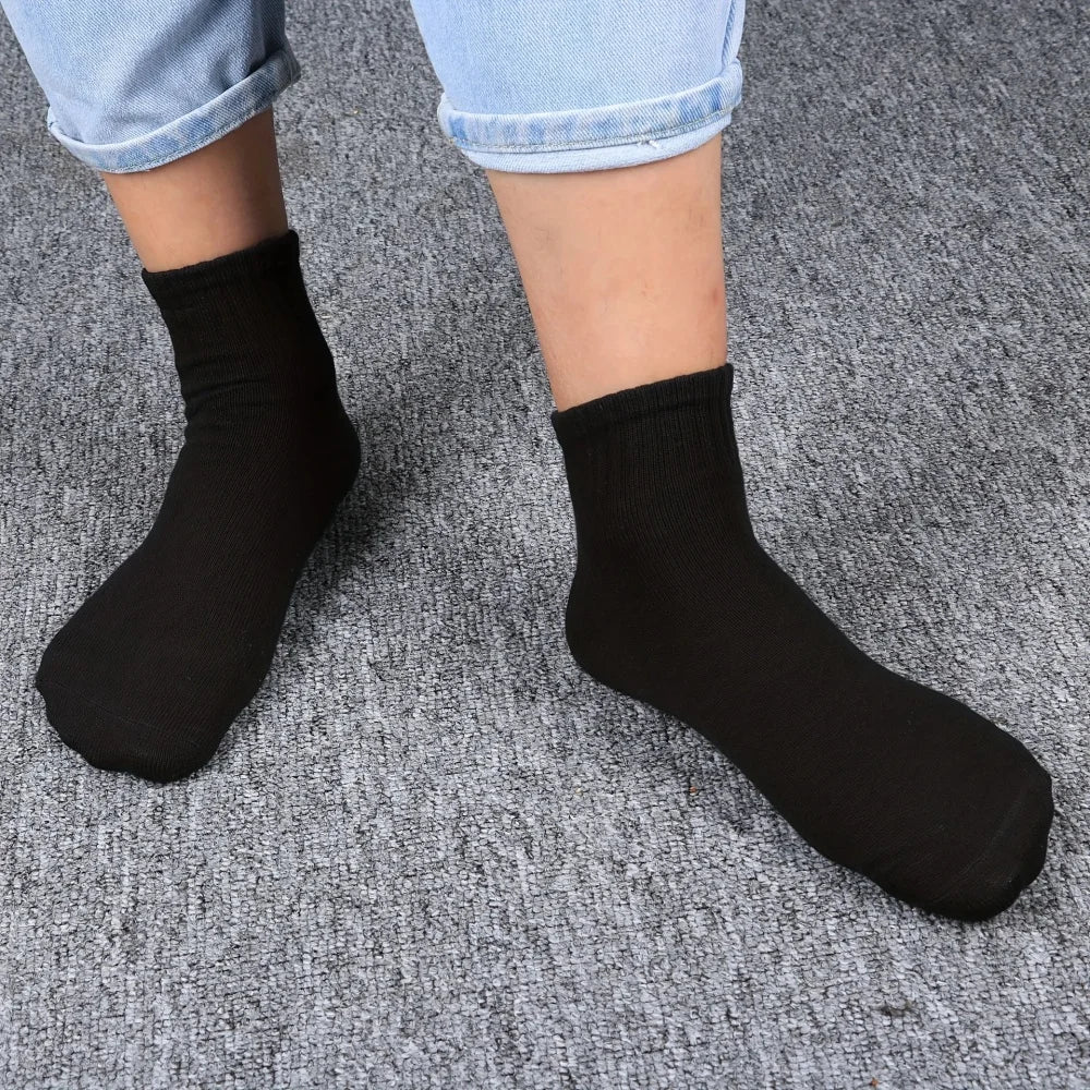 A pair of black mid-calf cotton socks worn by a person, displayed against a gray background.
