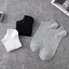 A collection of black and gray breathable men's sports ankle socks laid out on a gray surface.