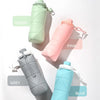 A collection of four collapsible silicone sports water bottles in green, pink, grey, and blue are displayed on a white backgr