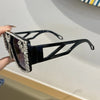 A pair of black geometric fashion sunglasses adorned with clear rhinestones, held by a hand.