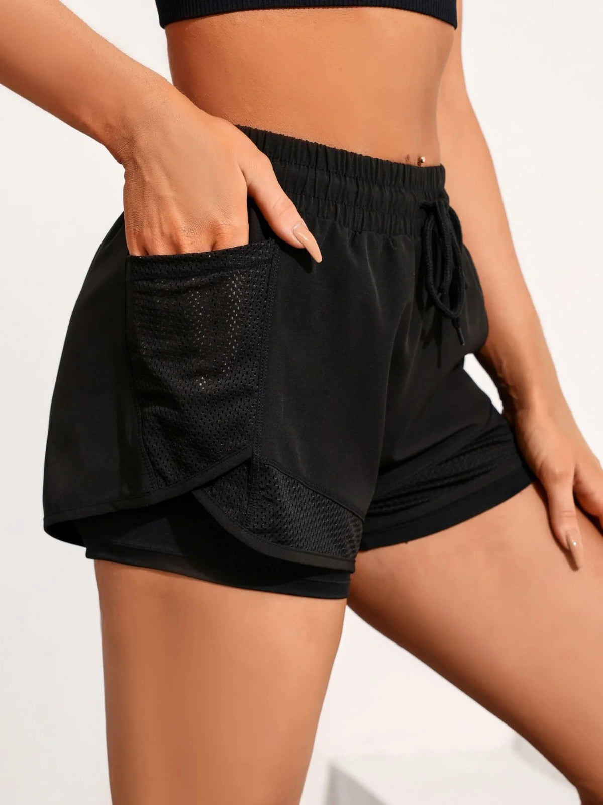 A woman wearing black athletic shorts with mesh pockets, showing the side pocket detail.