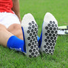 A pair of gray and blue athletic soccer socks with non-slip grip are lying on green grass.