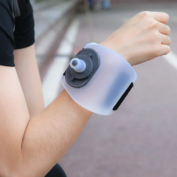 A hand is holding a clear silicone sports wrist water bottle device.