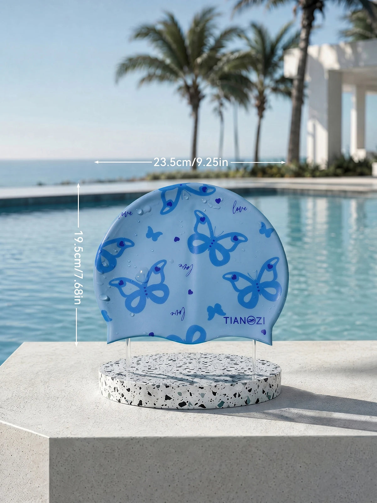 Light blue silicone swimming cap with a butterfly print resting on a white stone surface by the ocean.