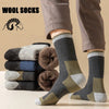 A person is wearing thick, patterned wool socks while standing, with a stack of similar socks nearby.