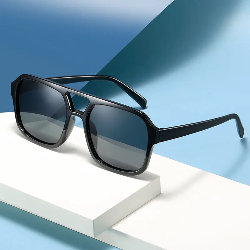 Schwarze Vintage-Sonnenbrille mit quadratischem Design auf weißem Untergrund vor blauem Hintergrund.