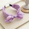 Purple paisley bandana headband tied in a bow resting on a light surface.