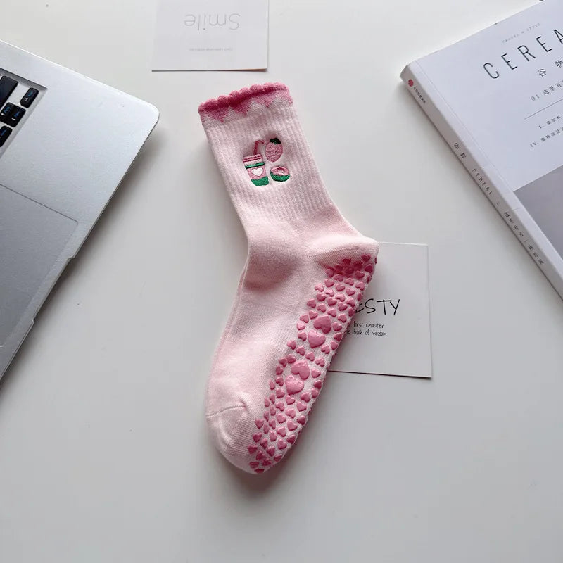 Chaussettes de yoga roses avec des cœurs brodés et une texture adhérente sur une surface blanche.