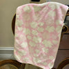 A pink and white coral fleece face towel draped over a wooden chair.