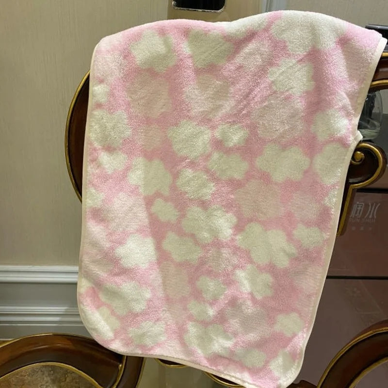 A pink and white coral fleece face towel draped over a wooden chair.