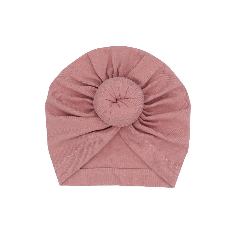 Ein fester, staubrosafarbener Baumwoll-Babyturban in Rosette-Form gefaltet.