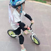 Un jeune enfant portant une chemise blanche et des protège-genoux/coudes, faisant du vélo avec des protections.