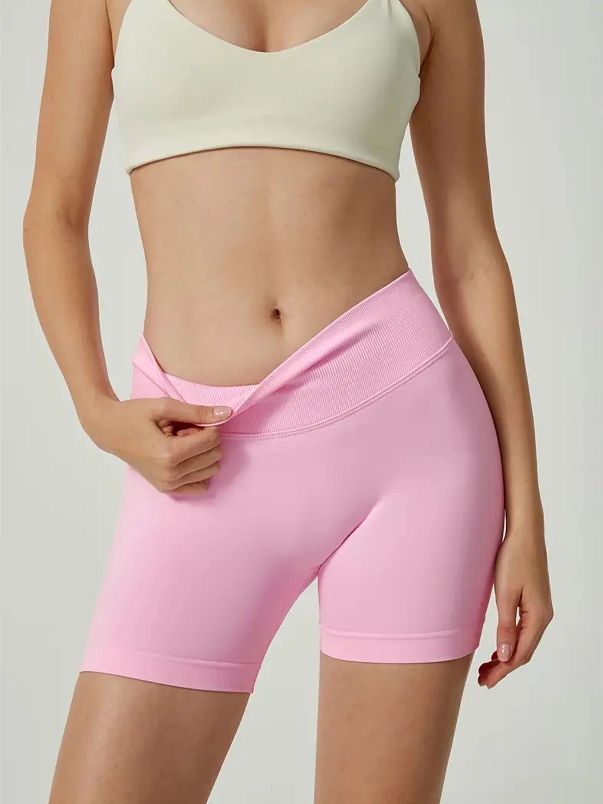 Un mannequin porte un short de yoga sans couture taille haute rose et un crop top crème.