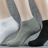 Un set de tres calcetines deportivos de algodón para el tobillo en blanco, gris y negro mostrados sobre una superficie.