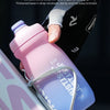 A hand holds a pink squeezable cycling water bottle with a non-slip groove design.