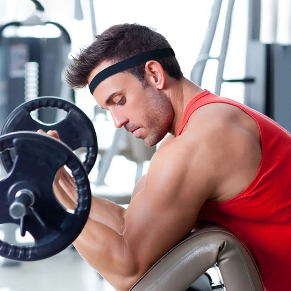 A muscular man wearing a black sports headband performs an exercise with a dumbbell in a gym setting.