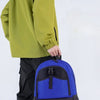 A young man wearing a lime green hooded jacket and black pants holds a blue multi-sport fitness backpack.