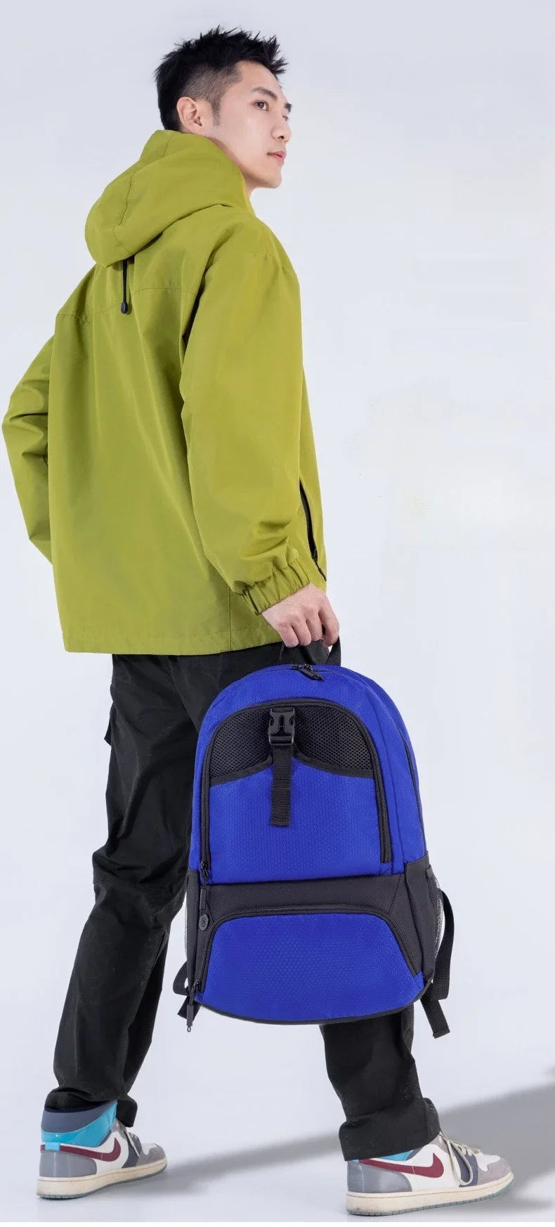 A young man wearing a lime green hooded jacket and black pants holds a blue multi-sport fitness backpack.