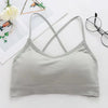 A light gray women's sports bra with thin straps is displayed on a white background next to some greenery and eyeglasses.