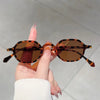 A hand holds a pair of vintage oval sunglasses with brown and black leopard print frames.
