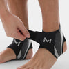 A person's foot is shown wearing black and gray compression ankle support foot sleeves.