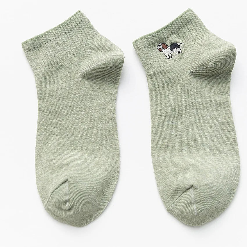 A pair of light green knitted cotton socks with a small black and white dog embroidery on the foot.