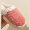 A close-up of cozy plush fleece slippers in pink and cream colors shown from the side.