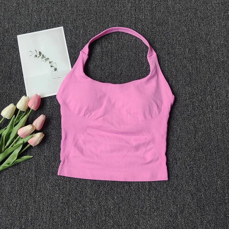 A bright pink seamless yoga and pilates sports bra is displayed on a dark gray fabric next to some pink tulips and a white ca